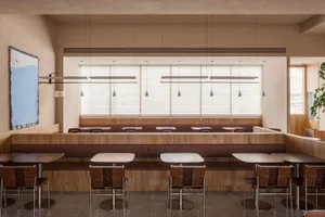 A modern restaurant interior design featuring wooden tables, concrete walls, and leather chairs.