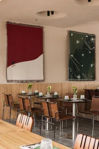 Modern restaurant interior with wooden walls and abstract tapestry hanging on the wall.