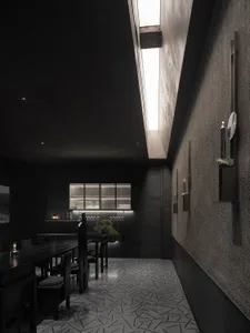 一間以深色工業風格為主的餐廳室內，擁有水泥牆面與地板、長形餐桌，以及簡約裝飾。