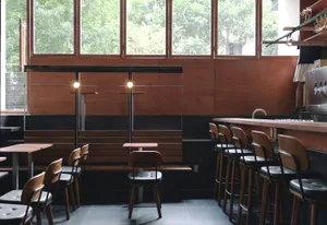 A modern cafe bar with wooden seating, leather stools, and metal accents.