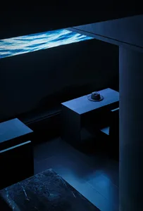 A modern, minimalist coffee shop interior with exposed concrete walls, a blue light, and a hat placed on a table.
