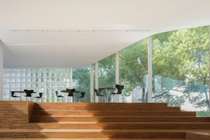 Modern restaurant interior with glass windows, wooden stairs, and tables set up for guests.