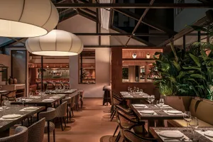 Modern restaurant interior with industrial design elements, featuring wood furniture, glass lighting, and greenery.