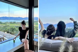 Two women sitting in front of a large glass window overlooking a scenic landscape with mountains and a lake.