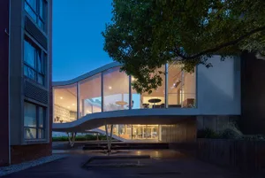 A modern restaurant exterior featuring a glass facade and a concrete structure, set against the night sky.