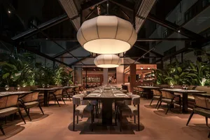 Modern restaurant interior with wooden tables, fabric chairs, and glass pendant lights.