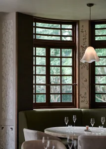 Modern restaurant interior with green booth seating, white marble table, and glass windows.