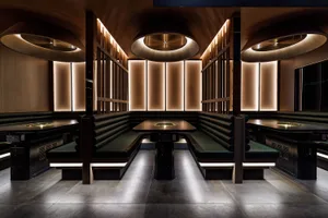 Modern restaurant booths with black leather seating, illuminated by warm, recessed lighting, and designed with sleek wood fur