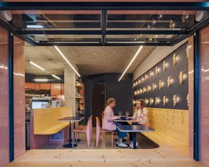 People sitting at a cafe with wooden tables, concrete columns, and terrazzo flooring.