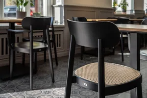 A cafe interior with wooden furniture, including black chairs with woven seats and wooden tables.