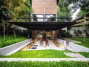 A modern restaurant exterior features a brick façade with a concrete patio surrounded by green plants.