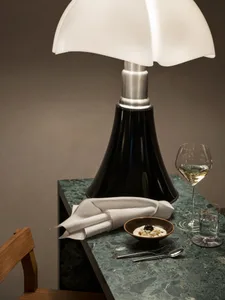 A modern restaurant table setting featuring a green marble table, a white shaded table lamp, a glass of white wine, a bowl of