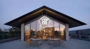 A modern rooftop cafe with glass walls, concrete flooring, and seating areas.