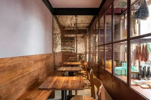 Interior view of a rustic restaurant cafe bar with wooden furniture, bar counter, and hanging meat products.
