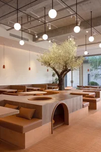 Modern cafe with minimalist design, concrete and wood materials, and a central tree.