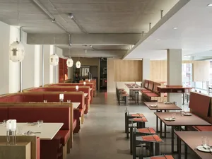 A spacious restaurant interior with modern design elements, including red upholstered booths and a concrete ceiling.