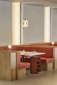 Modern industrial-style restaurant interior with red leather booths, white table, and geometric lighting fixture.