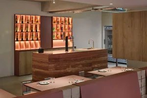 A modern bar with a marble counter featuring illuminated shelves filled with various bottles.