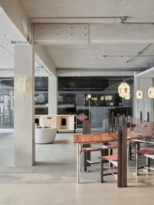 An interior view of a modern minimalist cafe with concrete walls, wooden tables, and hanging light fixtures.