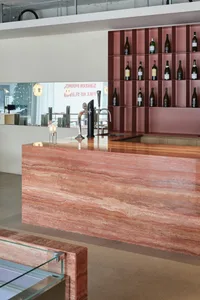 A contemporary bar with a reddish marble countertop and a shelving unit displaying wine bottles.