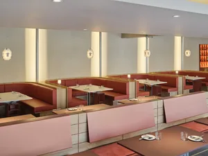 A modern restaurant interior featuring red booth seating with wooden accents and glass pendant lights.