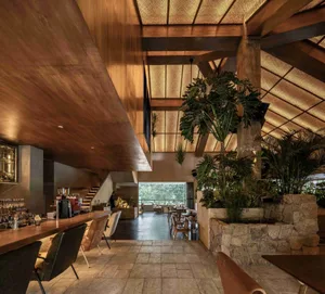 A modern restaurant with a wooden ceiling, stone bar, and concrete flooring, featuring a concrete bar counter and stone walls