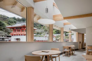 Modern cafe interior with wooden furniture and architectural details overlooking a traditional Japanese temple.