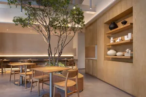 A modern restaurant cafe interior with wooden furniture, featuring a central tree and display shelves.