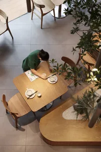 A modern restaurant interior with wooden tables and chairs, green plants, and white porcelain dinnerware.