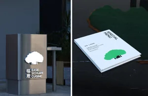 A minimalist metal menu stand with a green tree logo and a white menu cover featuring a tree logo on a black marble counter.