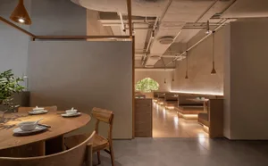 A modern restaurant interior featuring wooden tables and chairs, contemporary lighting, and a minimalist design aesthetic.