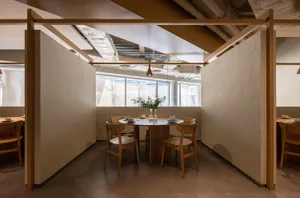 A modern restaurant interior designed with wooden tables and concrete flooring, featuring a round table, chairs, and minimali