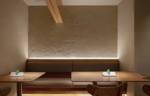 A modern restaurant interior with wooden tables and benches, featuring a textured wall and ambient lighting