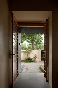 A traditional Japanese entrance featuring a wooden door with shoji panels, surrounded by greenery and a stone lantern.