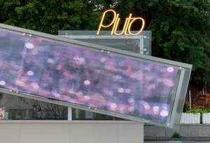 Neon Pluto sign and digital display on an exterior storefront extension