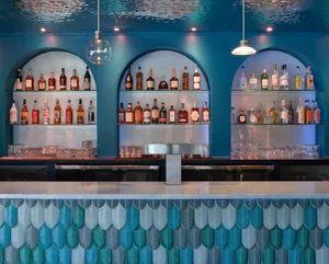 A photograph of a modern bar counter featuring glass shelves with various bottles of liquor.