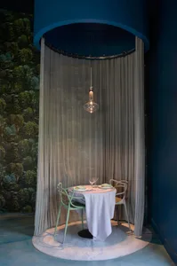 A modern restaurant booth with a white tablecloth, green chairs, and a fabric curtain.