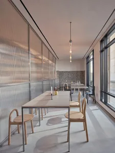 Modern restaurant interior with wooden tables and metal chairs seen through glass doors.