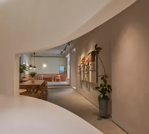 A cozy cafe interior with concrete floors and walls, featuring a white table and chairs, and a display of bags and cards on t