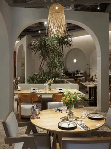 Modern restaurant interior with wooden tables, glass vases, and plush fabric chairs.