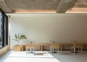 Modern minimalist cafe interior with wood seating and concrete ceiling.