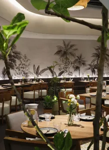 Lushly decorated cafe with wooden furniture and plant life on tables and walls.
