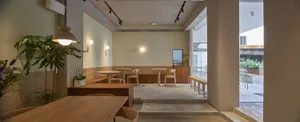 A modern restaurant interior featuring wooden tables, glass partitions, and a concrete floor