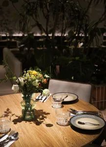 A table set for dining in a modern restaurant, featuring wooden elements and a vase of flowers.