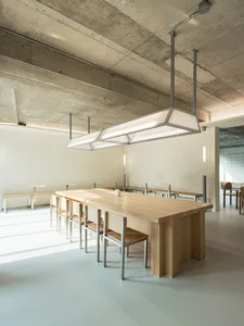 Modern restaurant interior with minimalist design featuring wood tables, metal chairs, and concrete ceiling.
