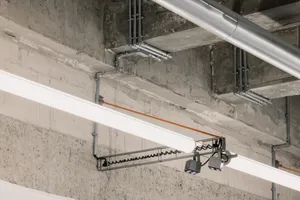 Lighting fixtures mounted on a concrete ceiling with exposed pipes and ducts.