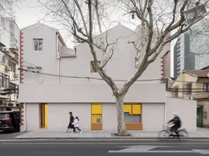 一棟現代住宅的街景，擁有混凝土外牆、黃色窗框，以及前方一棵樹。