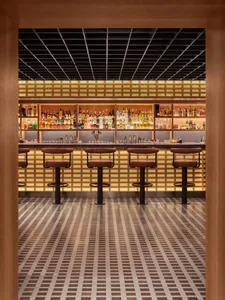 Modern bar with tiled floor, stools, and backlit shelves filled with various bottles of alcohol.