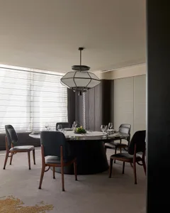 A modern dining room featuring a round table with chairs made of wood and leather, under a geometric chandelier.