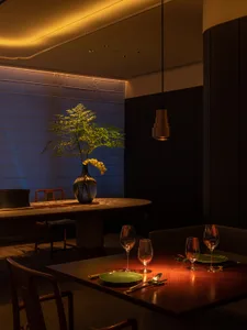 A modern restaurant interior with wooden furniture, green plates, and a vase with flowers on a table.
